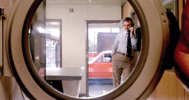 A scene from the movie Duel where a man is talking on a land line framed by a circular window